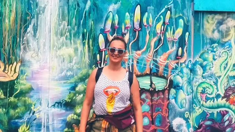 A girl wearing dark brown tights. She's at the festival. Graffiti in the background. She had anxiety and depression. Smiling.