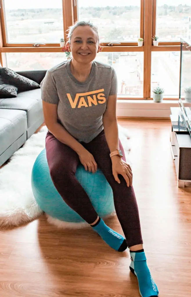 a white woman in her early 30s sitting on a fitness ball, looking at the camera and smiling