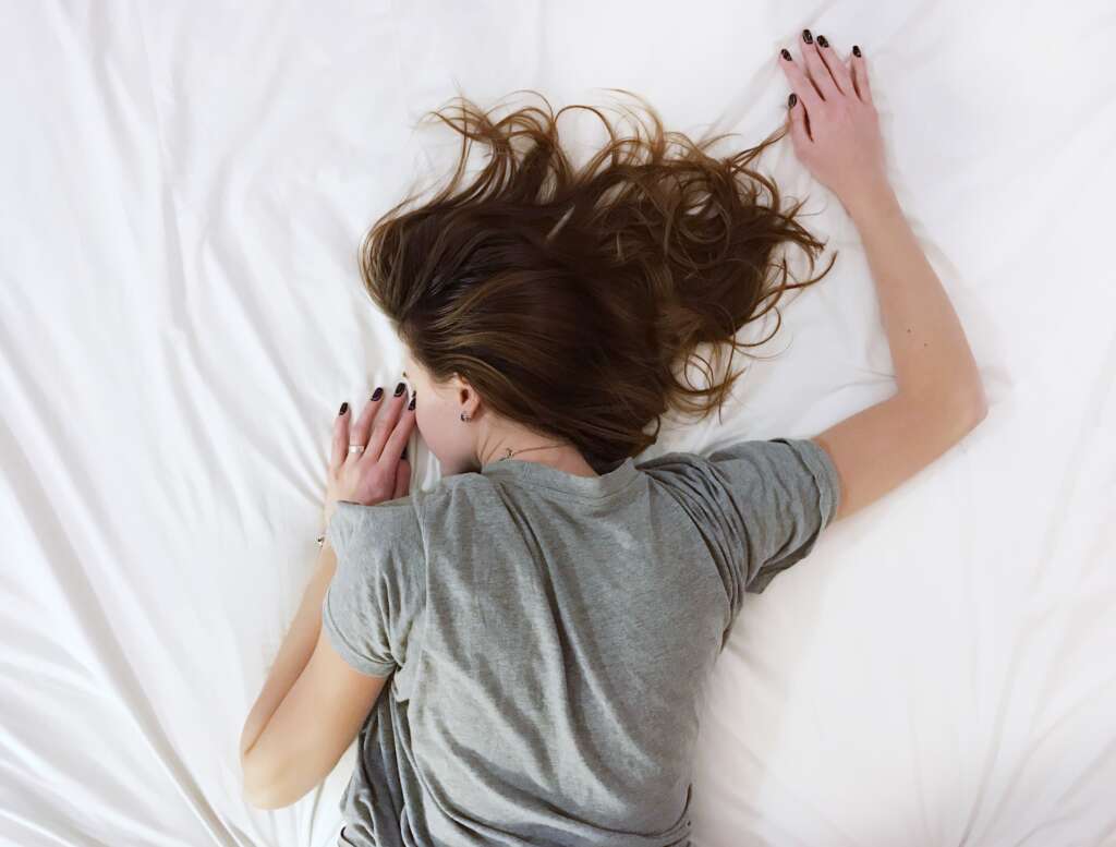 a girl is lying on a bed face down. Her right arm is up and her left arm is bent by her side.