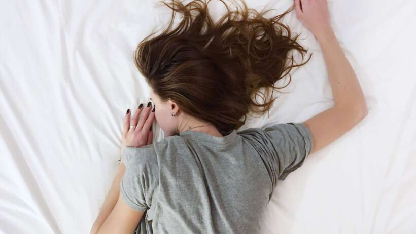 a girl is lying on a bed face down. Her right arm is up and her left arm is bent by her side.